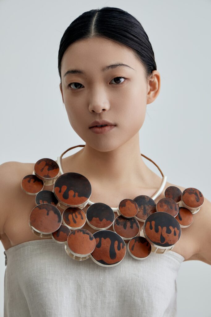 This piece is made from sterling silver, calabash, and dyed persimmon. It continues the use of circular repetition to express recurring reflective emotions.