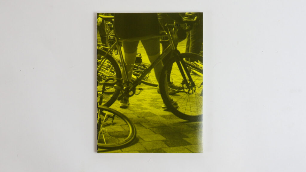 Cover of yellow book featuring a photograph of overlapping bicycle wheels and legs, shot from a low angle.