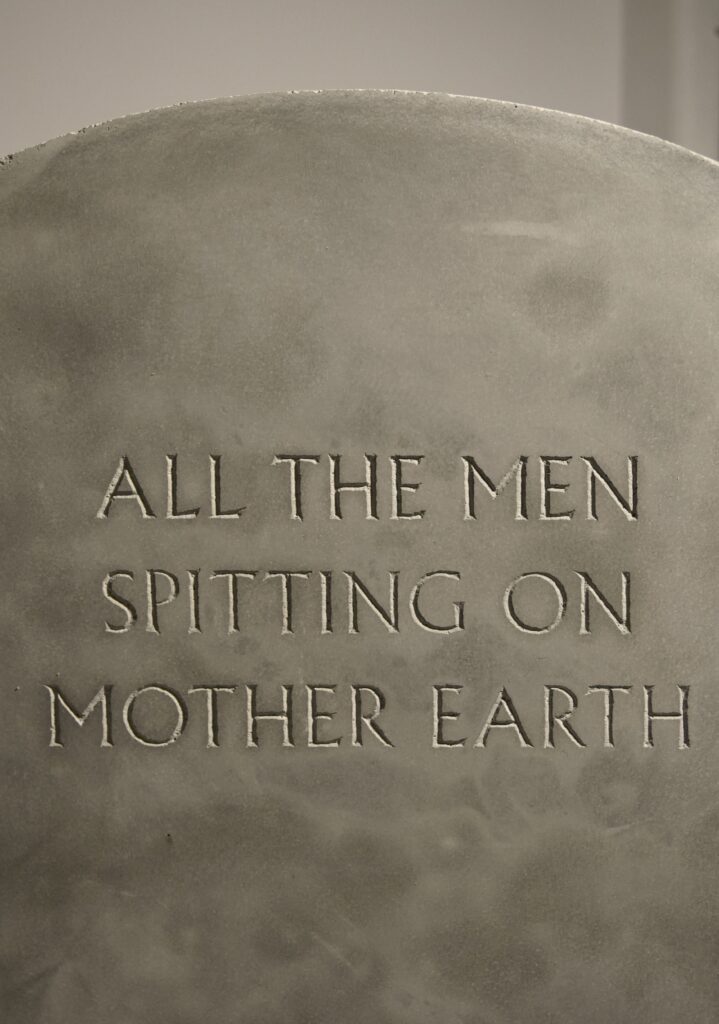 Hand-engraved text in concrete reading 'all the men spitting on mother earth'