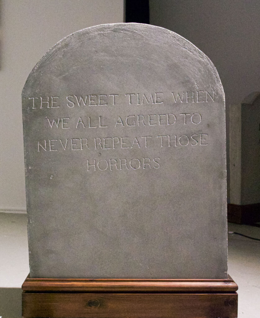 Round gravestone reading 'The Sweet Time When We All Agreed to Never Repeat Those Horrors'