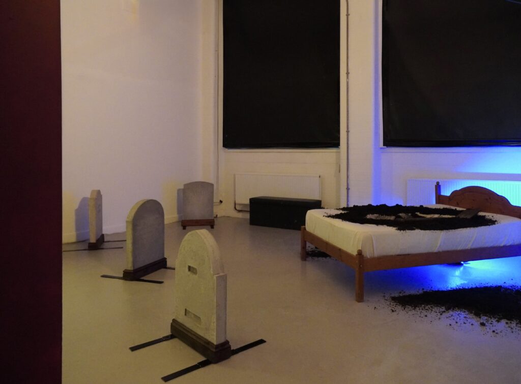 A bed with earth spilling out of it, facing four gravestones.