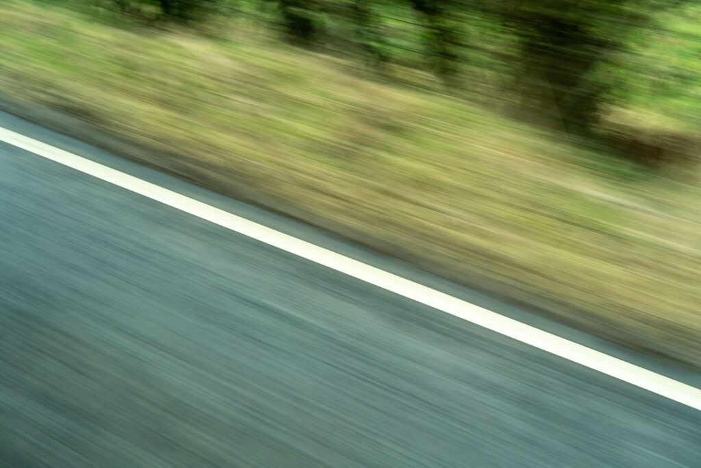 Blurred image of grass and road markings taken from a moving vehicle.