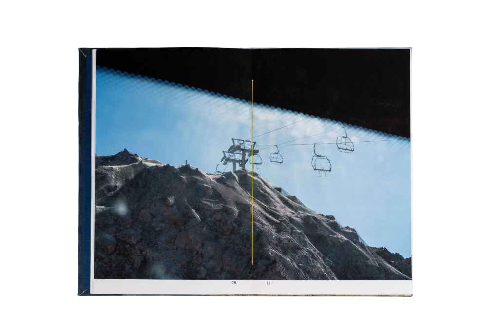 A full-bleed image across two pages showing a ski lift suspended over rocky terrain, photographed through a patterned coach window.