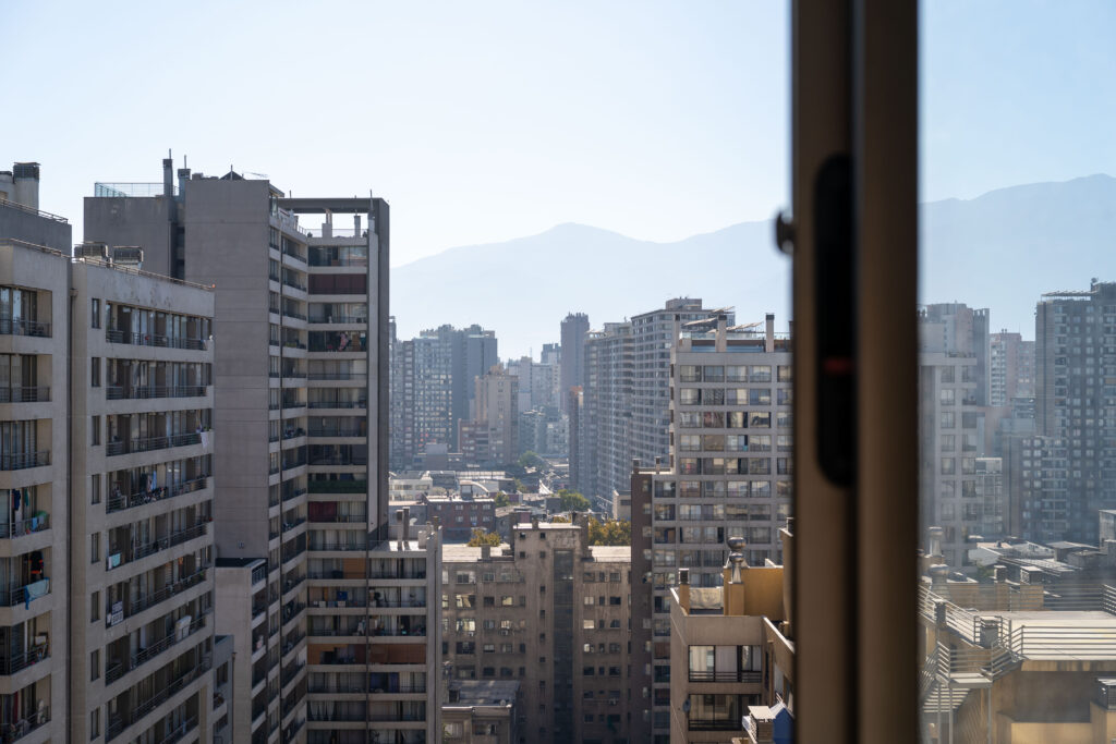 View through a glass door of a high-rise apartment, looking out over Santiago’s dense skyline with mountains in the distance.